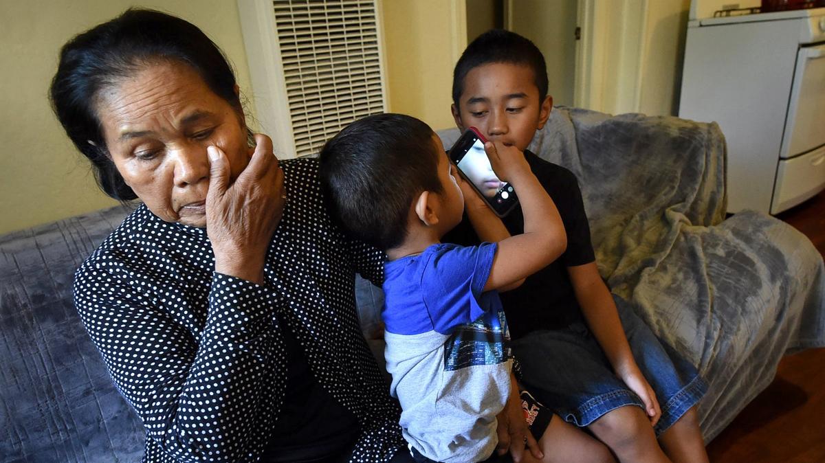 Peck Loek, whose son and son-in-law were deported to Cambodia in June, wipes away tears inside her Fresno apartment as she tends to ger grandsons in August.