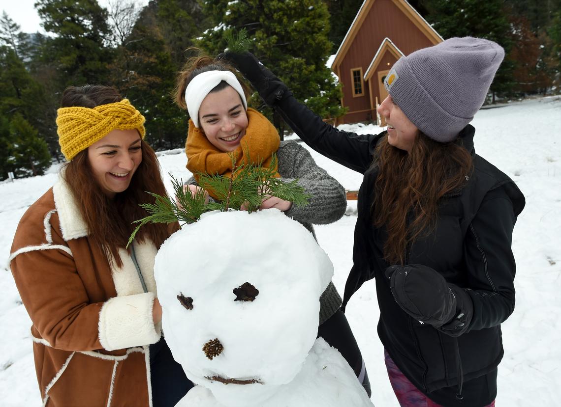 Massachusetts native Jasmine Scalli, now of San Diego, right, with friends Marie Foltier, left, and Anne Pervier, center, both of France, all on their first visit to Yosemite, have fun building a snowman in front of the chapel in Yosemite Valley, Tuesday, Dec. 4, 2018.