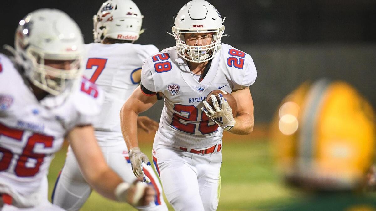 Buchanan’s Caden Rodgers, center, waits for blocking before charging though the scrimmage line on a run up the middle during their game against Kingsburg at Kingsburg High on Friday, Aug. 20, 2021.