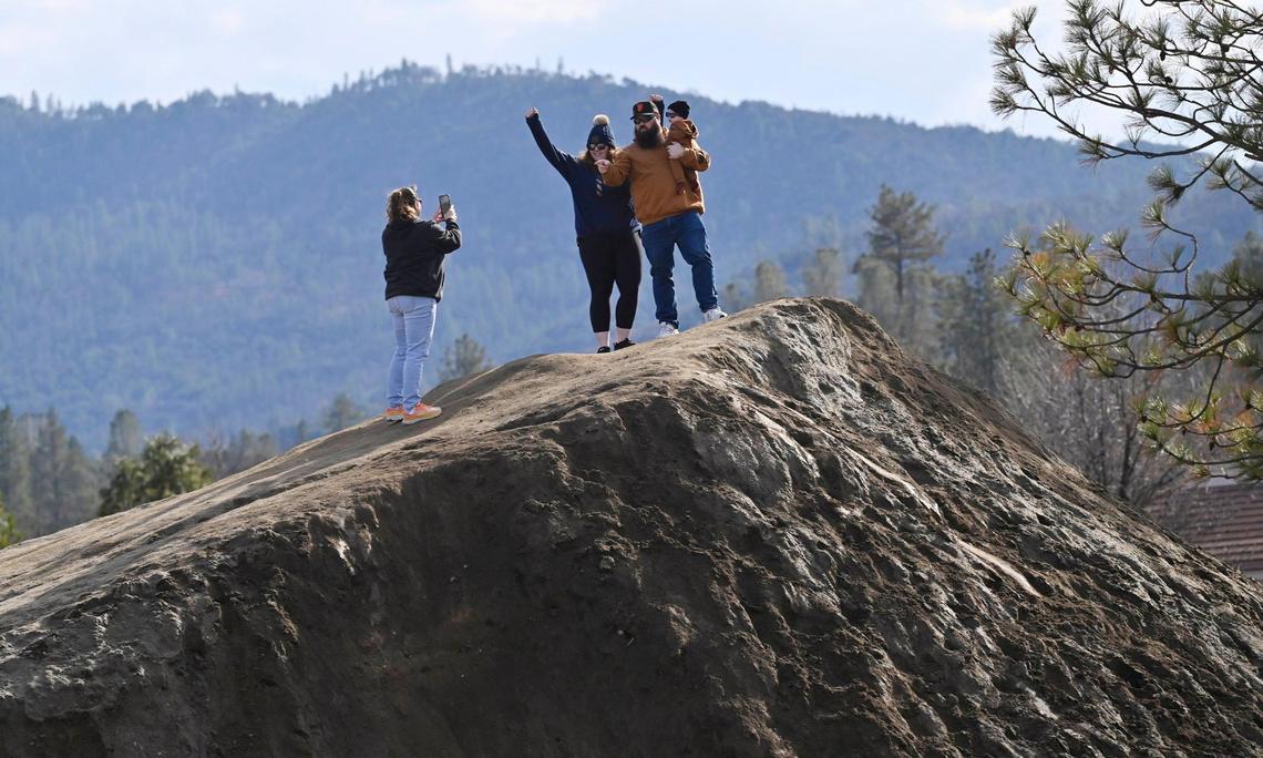 LeShawn Lucas, far left, photographs Jamie and Skyler Gamblin holding their child Hunter Gamblin, 6 months, on top of the 20-foot dirt mount dubbed Mt. Chipotle Friday, Jan. 3, 2025 in Oakhurst. The family had been following social media posts about the mound and just had to see it today. The mound located next to a new Chipotle Mexican Grill may be permanently removed in a few days but until then the community of Oakhurst and others from around the Valley are enjoying the dirt made famous in social media posts.