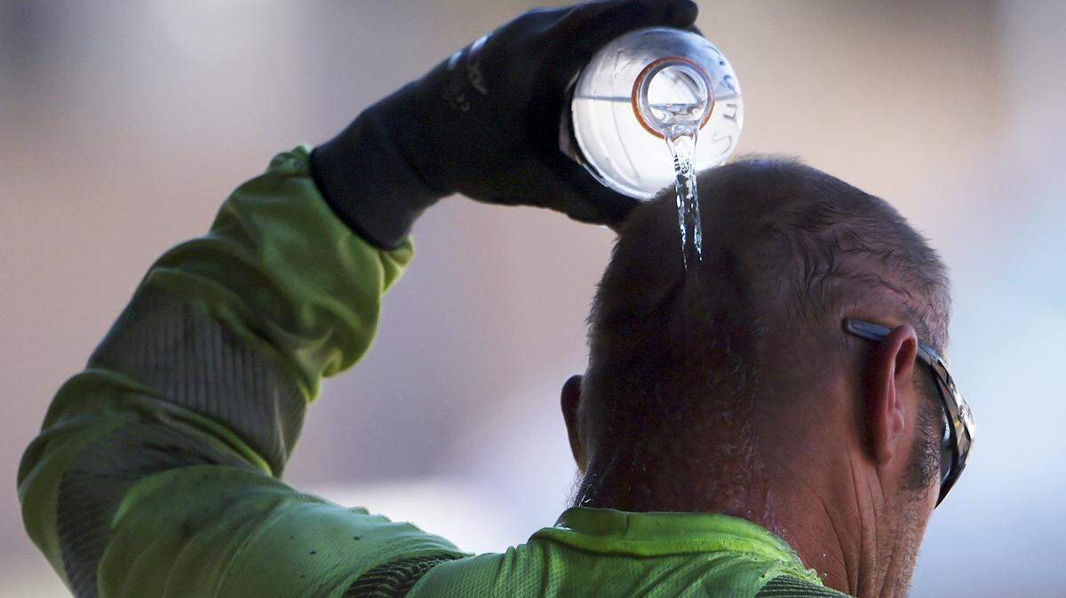 A construction worker pours water over his head to cool off in the shade at the end of hot work day in Fresno.