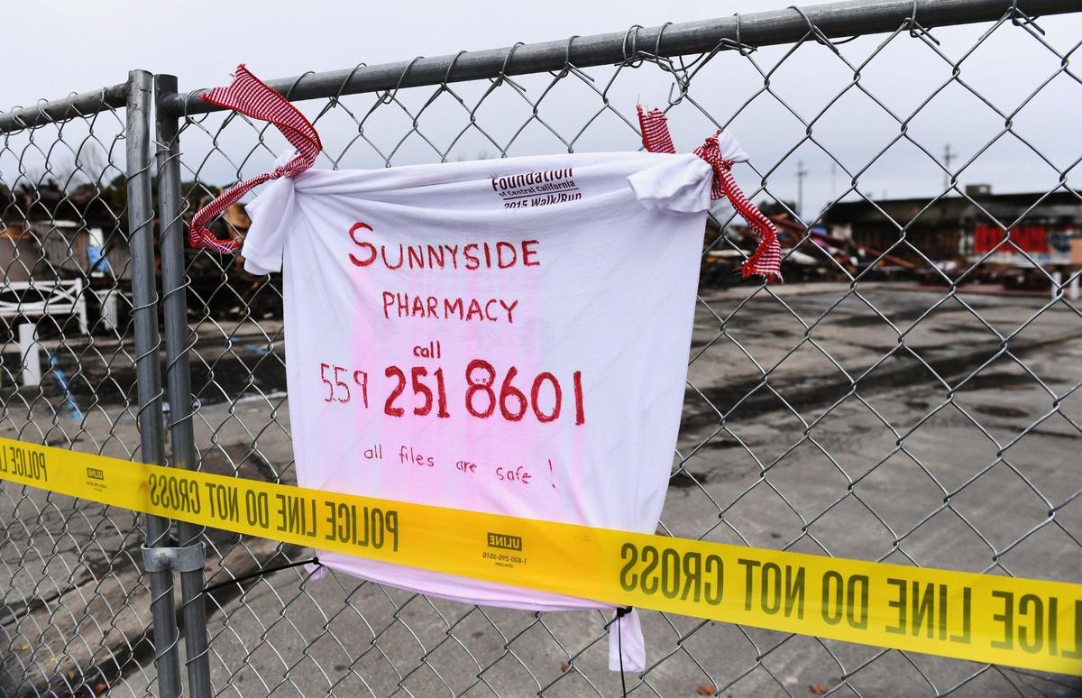 A t-shirt is tied to fencing with contact info for Sunnyside Pharmacy customers after a fire destroyed the building which also housed Sunnyside Delicatessan. Photographed Wednesday, Jan. 11, 2023 in Fresno.