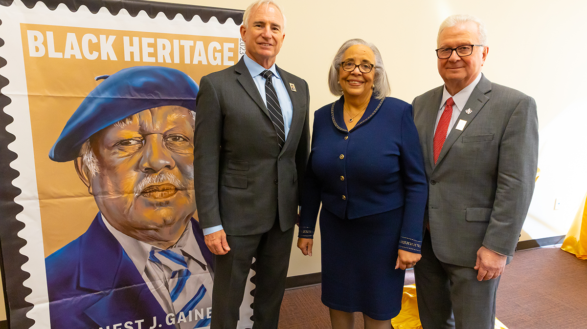 From left, Donald L. Moak, U.S. Postal Service Board of Governors, Dianne Gaines, widow of Dr. Ernest J. Gaines, and Dr. Joseph Savoie, University of Louisiana-Lafayette president, are shown beside an image of Dr. Gaines’ postage stamp.