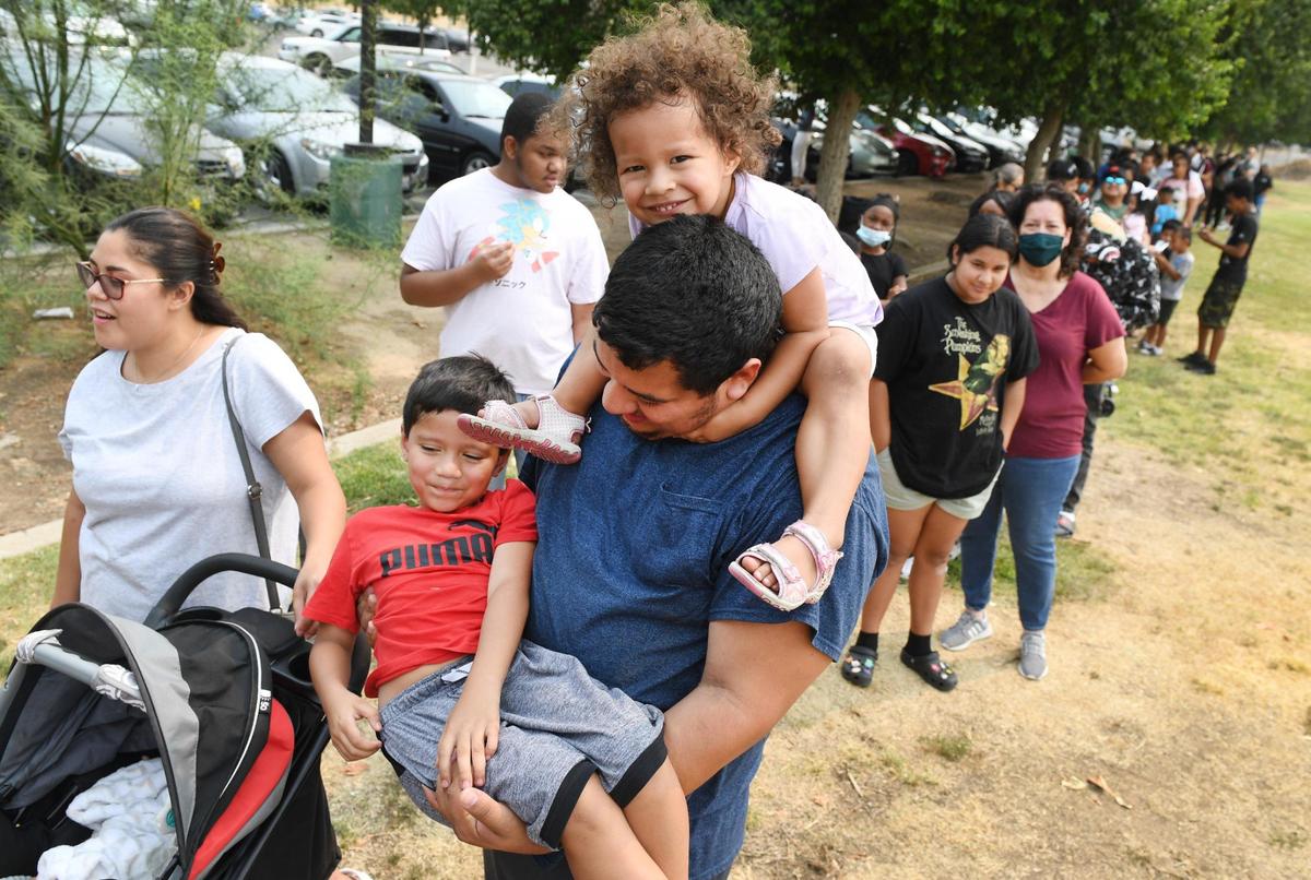 Families wait in line at Cary Park in Fresno before the start of the Community Kick it Outreach shoe giveaway on Saturday, Aug. 7, 2021. This is the fourth annual shoe giveaway organized by Pastor Edward Thomas of Living World International Church in Fresno to provide footwear for families in need before the start of the school year.