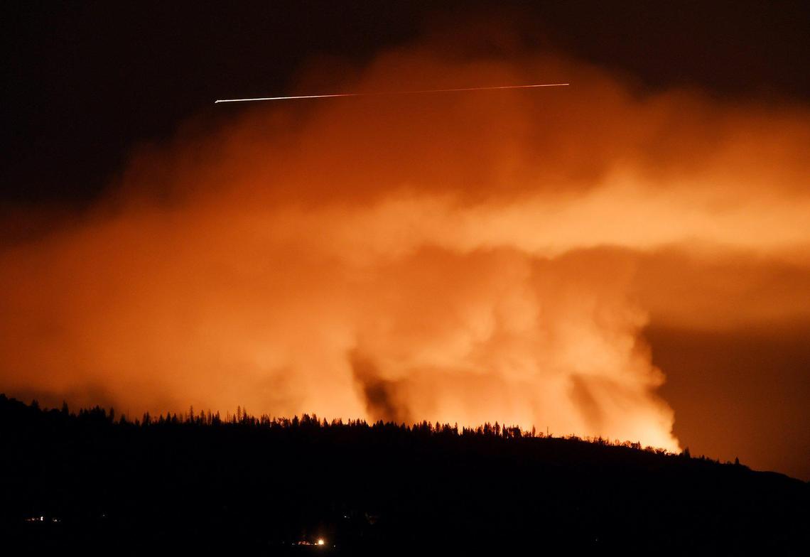 A plane, in a 30 second exposure, travels high above the orange glow of the Blue Fire south of Shaver Lake Tuesday night, June 29, 2021 near Tollhouse.