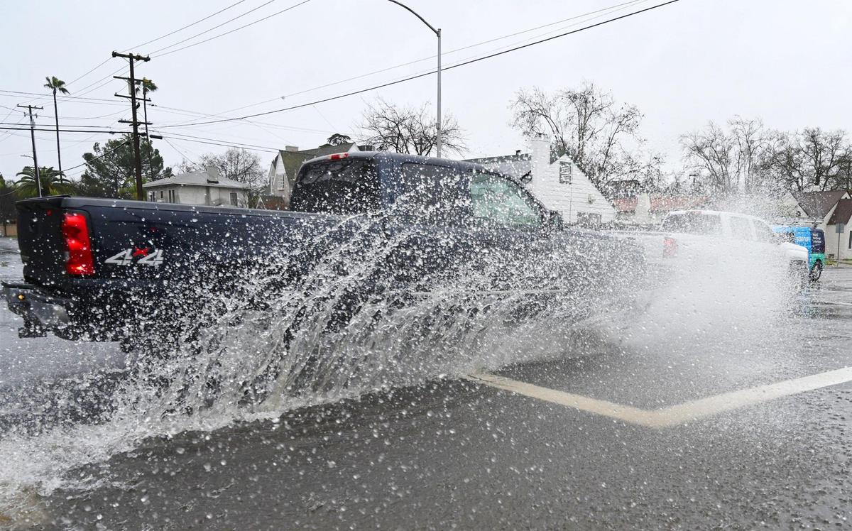 Westbound traffic along Clinton Avenue splashes through the flooded intersection at Maroa Avenue as in central Fresno as an atmospheric river storm continues to dump rain on Monday, Jan. 9, 2023.
