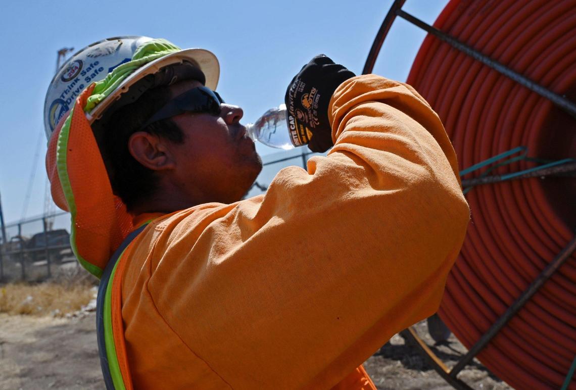 Jorge Bacerra takes a drink of water from a bottle in his vest as the temperature reaches 106 degrees along Weber Avenue near Roeding Park in September 2022.