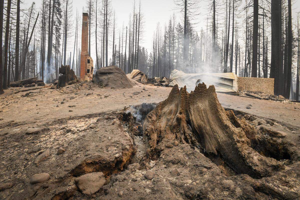 A tree stump smolders in front of a burned cabin in the Camp Silver Fir area on the north of Huntington Lake on Sunday, Sept. 13, 2020. Fire officials said a fire tornado blew through the area at some point last week burning cabins and knocking down many trees.