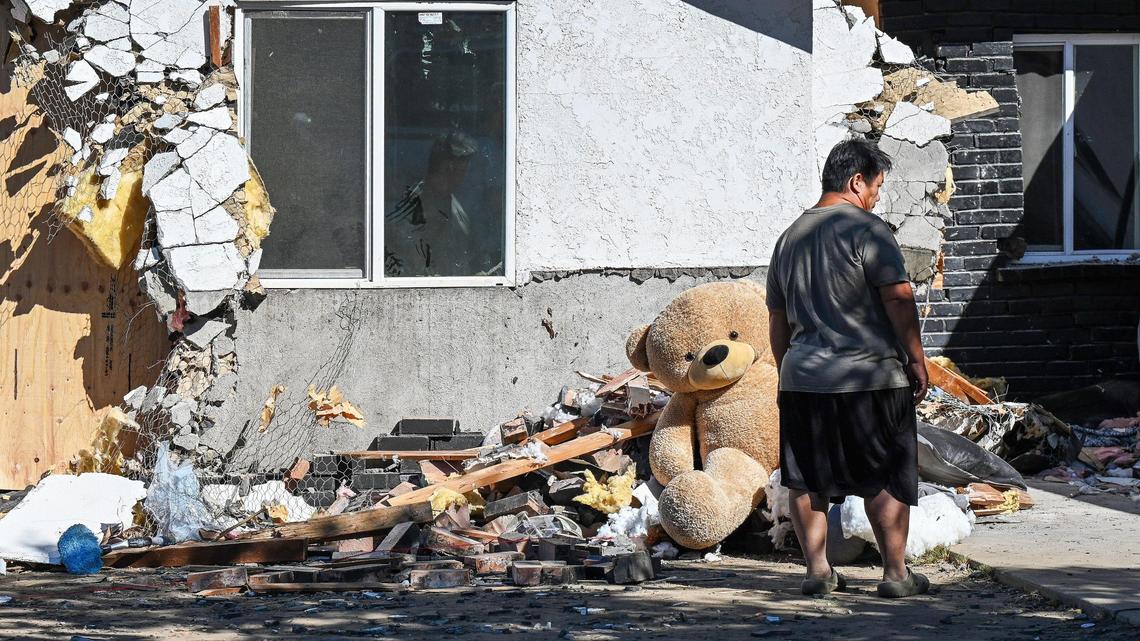 A family member stands near a large stuffed bear sitting amongst the damage a home at the corner of Cedar and Nevada avenues in Fresno on Thursday, Oct. 17, 2024 after a vehicle crashed into the home killing two people during a pursuit on Wednesday night.