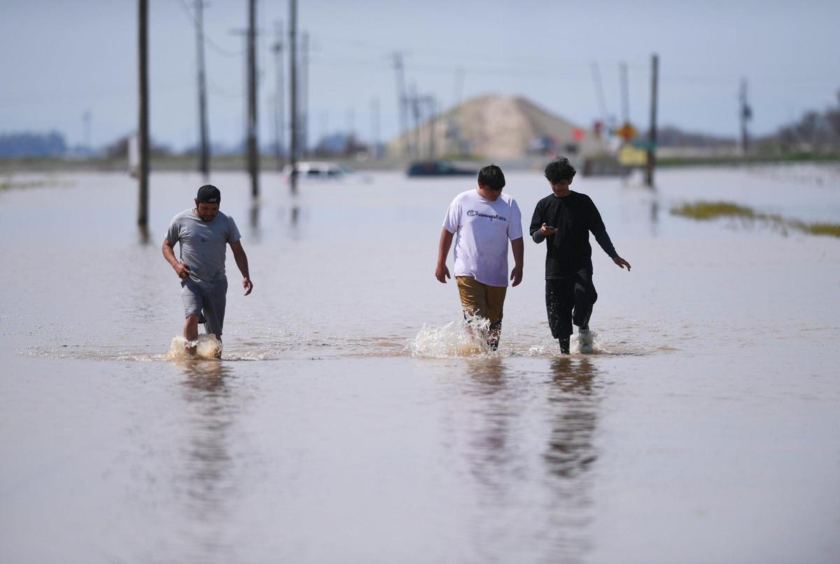 Alpaugh’s Giovanni Villa, left, Rodrigo Villa, center, and Octavio Villa, right, walk eastward along a flooded Avenue 56 from Highway 43, seen in the background running left to right, Saturday afternoon, March 18, 2023. The three rode their bikes from Alpaugh just to see the flooding at the intersection about 3 miles north of Allensworth State Park.