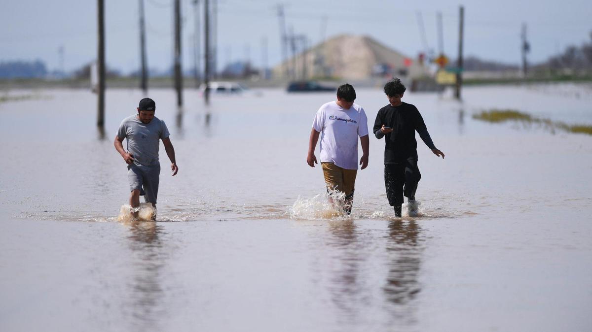 Alpaugh’s Giovanni Villa, left, Rodrigo Villa, center, and Octavio Villa, right, walk eastward along a flooded Avenue 56 from Highway 43, seen in the background running left to right, Saturday afternoon, March 18, 2023. The three rode their bikes from Alpaugh just to see the flooding at the intersection about 3 miles north of Allensworth State Park.
