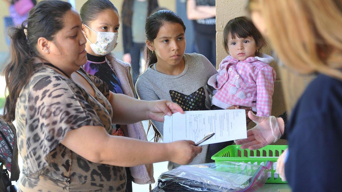 Rosa Martinez, left, turns in paperwork at Addams Elementary to receive laptops for her daughters, Maria Martinez, 12, in mask, and Laura Martinez, 10, holding their 1-year-old sister, Sofia Martinez, during Fresno Unified’s distribution event at Addams, Wednesday April 22, 2020. The district is providing a laptop to every student in fourth through 12th grade and a tablet to every student in pre-k through third grade, to ensure that students stay connected during the COVID-19 pandemic closure. Addams is distributing a little over 900 devices to their students.