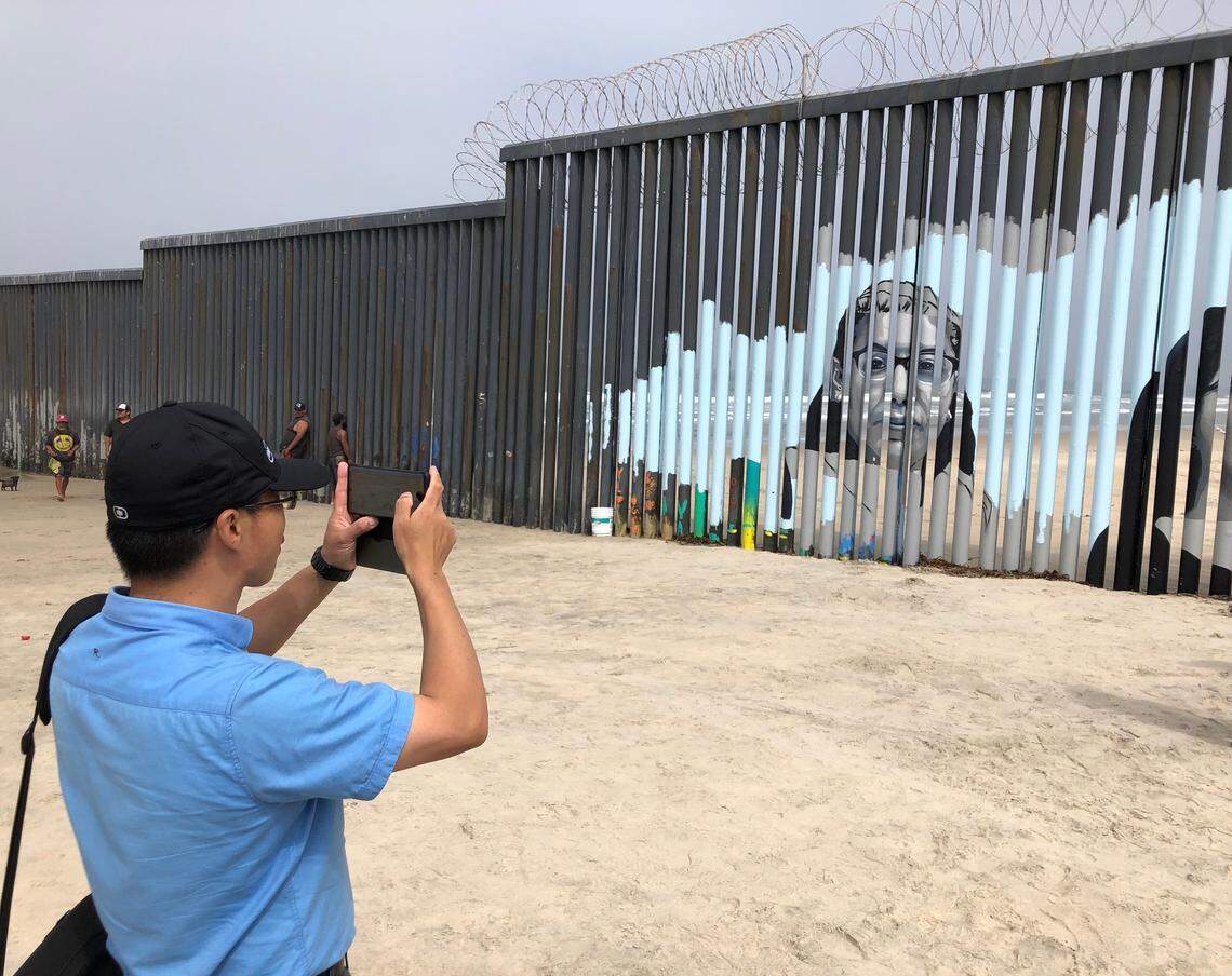 Visitors view a new mural displayed on the Mexican side of a border wall in Tijuana, Mexico, Friday, Aug. 9, 2019. The mural shows faces of people deported from the U.S. with barcodes that activate first-person narratives on visitors’ phones. Lizbeth De La Cruz Santana conceived the interactive mural in Tijuana as part of doctoral dissertation at the University of California, Davis. (AP Photo/Elliot Spagat)