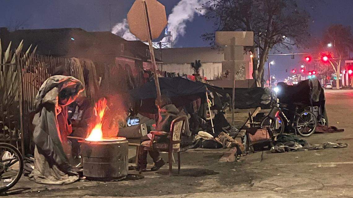 Some unhoused people sit next to a warming fire on Santa Clara Street in downtown Fresno.