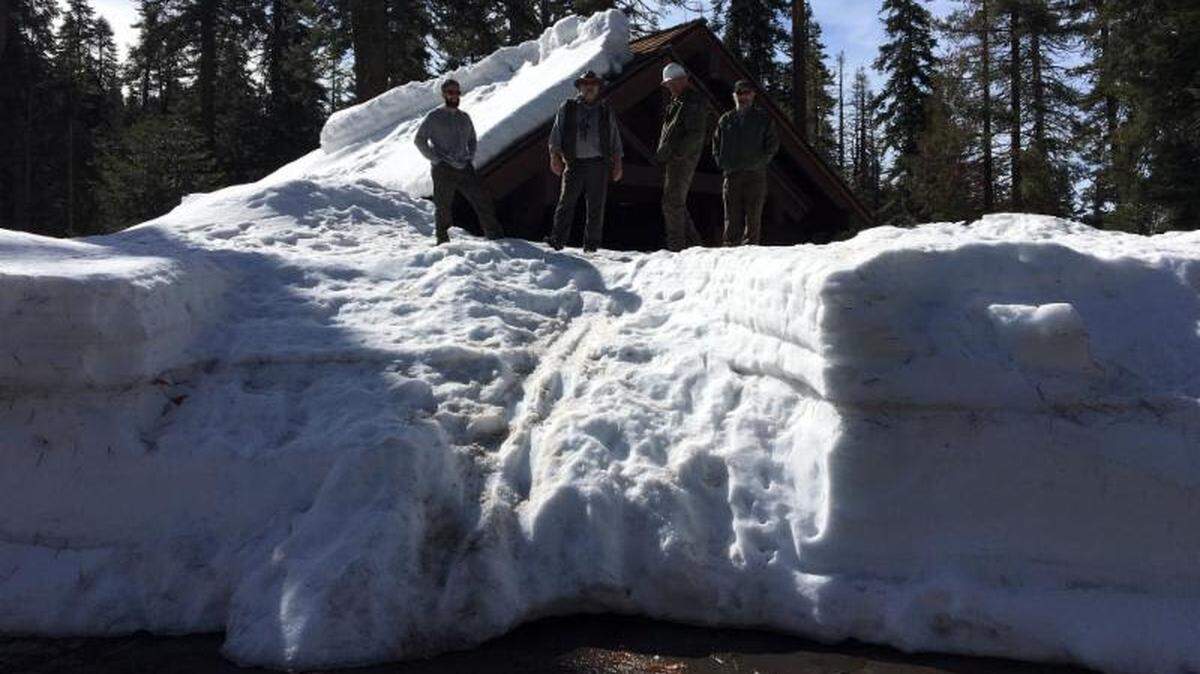 Rangers stand on the snow at the Sherman Tree comfort station.