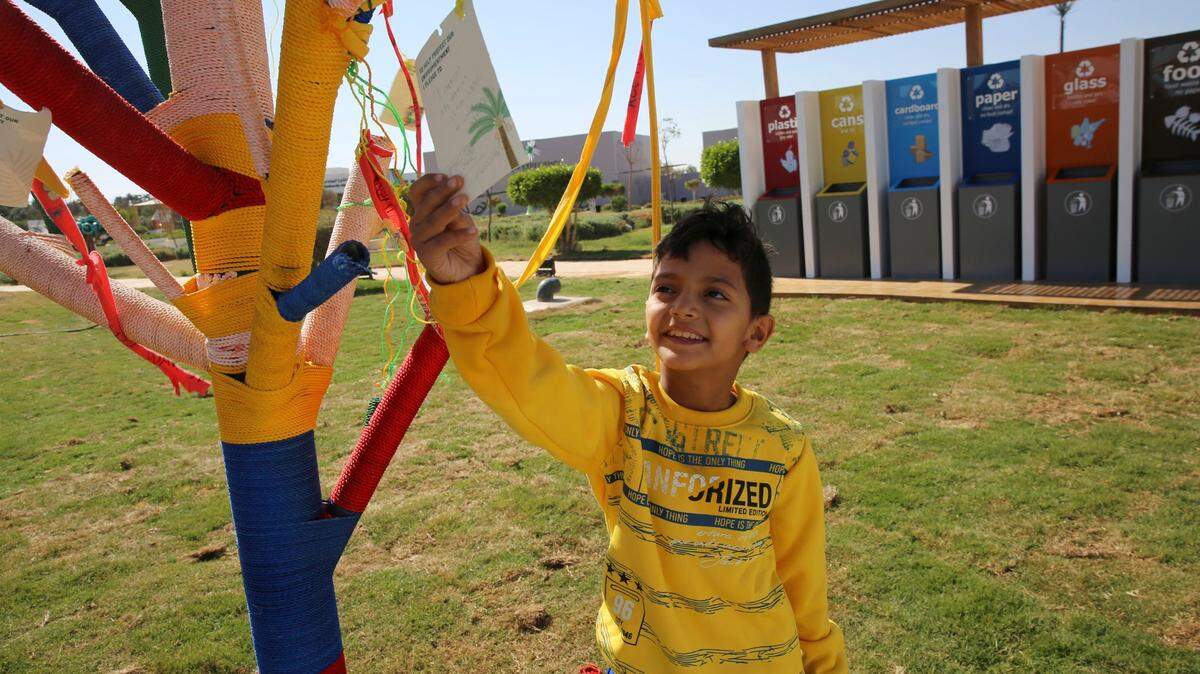 An Egyptian boy reads a note posted on an artificial tree set up for people to hang a note saying what promise they will make to help fight climate change, in the Green Zone of the COP27 U.N. Climate Summit, in Sharm el-Sheikh, Egypt, Friday, Nov. 18, 2022.