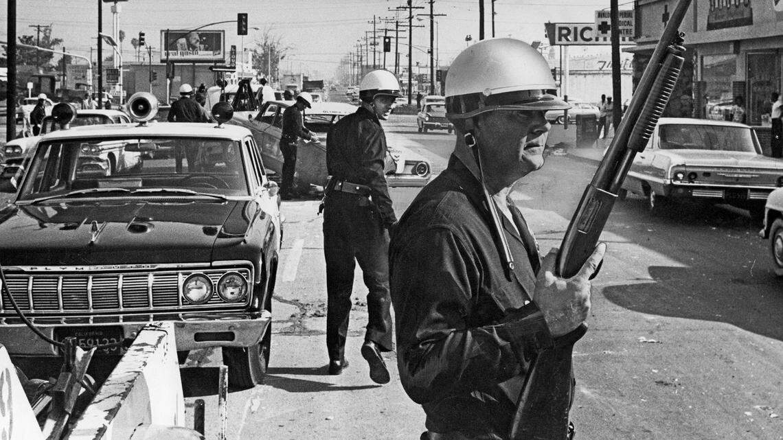 Los Angeles police officers stand guard as debris from a day of violence is cleared from the intersection of Avalon Boulevard and Imperial Highway, one of the worst trouble spots from which violence was spreading, on Aug. 13, 1965.