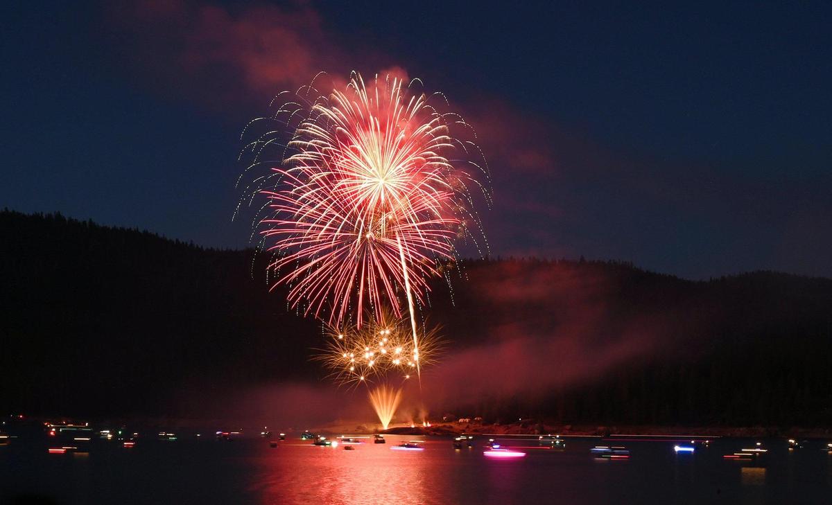 A flotilla of colorfully-lit boats floats on the lake watching the show as smoke begins to fill the sky at the 2022 Shaver Lake fireworks Saturday, July 2, 2022 at Shaver Lake. A parade of about a dozen decorated boats started at 6pm, cruising in front of the spectators before the fireworks show which began at dark. Thousands came to celebrate the holiday, chasing parking spots along Highway 168 and side streets creating congestion.