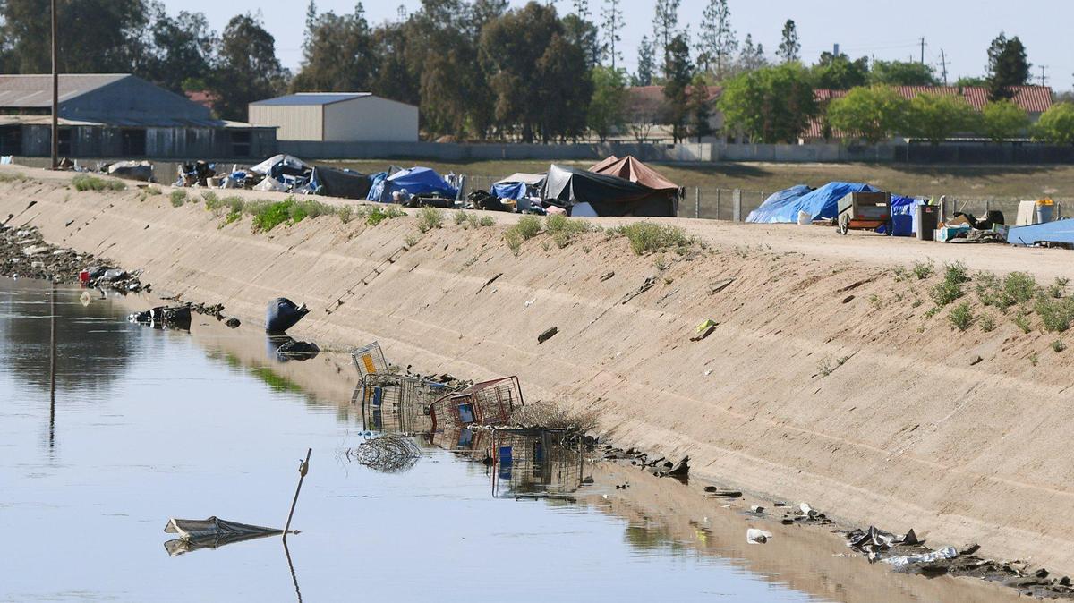 Homeless camps and trash clutter a canal north of Dakota Avenue, just west of Palm Avenue, in Fresno on April 2, 2021. A grand jury investigation in 2019-20 found Fresno County and the city of Fresno’s responses to homeless people lacked oversight and transparency.