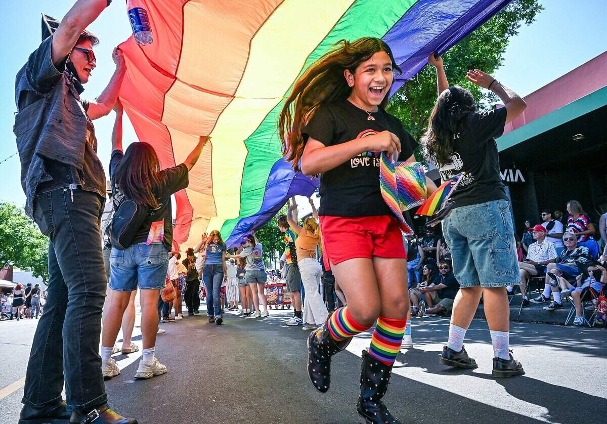 Parade goers run beneath a a giant Pride flag carried by participants from the First Congregational Church of Fresno, known as the Big Red Church, during the annual Fresno Rainbow Pride Parade and Festival in the Tower District on Saturday, June 6, 2026.