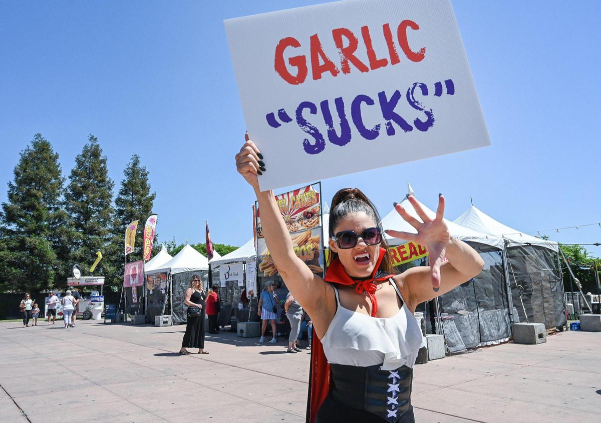 “Lady V” one of several vampires wandering about the Fresno Fairgrounds, holds up a sign protesting garlic, considered to be a vampire deterrent, on day one of the National Garlic Festival at the Fresno Fairgrounds on Friday, May 13, 2022.