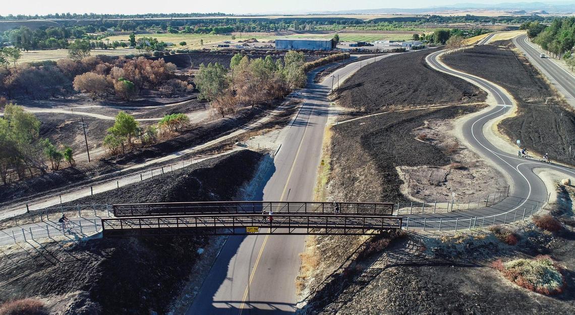 A drone photo shows the Rice Road pedestrian bridge on the Eaton Trail and the Republic Services recycling center at top center on Rice Road near Friant Road just north of Fresno on Wednesday, June 23, 2021. Recent fires around the recycling center have blackened a number of acres of the San Joaquin River bottoms area and the Eaton Trail.