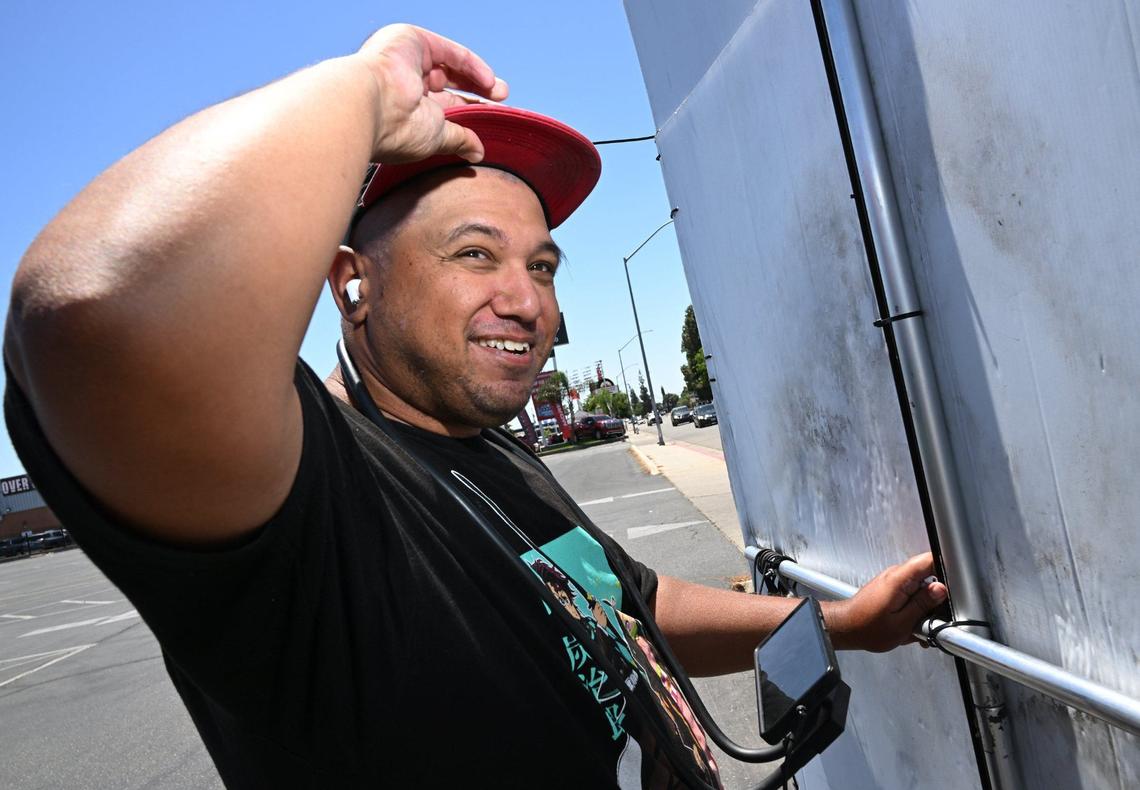 Gabriel Carpio talks about how he shaves his head to help keep cool while working along Blackstone Ave. advertising for USA Furniture by standing with a sign and twisting it back and forth along the sidewalk. Photographed Wednesday, May 29, 2024 in Fresno.