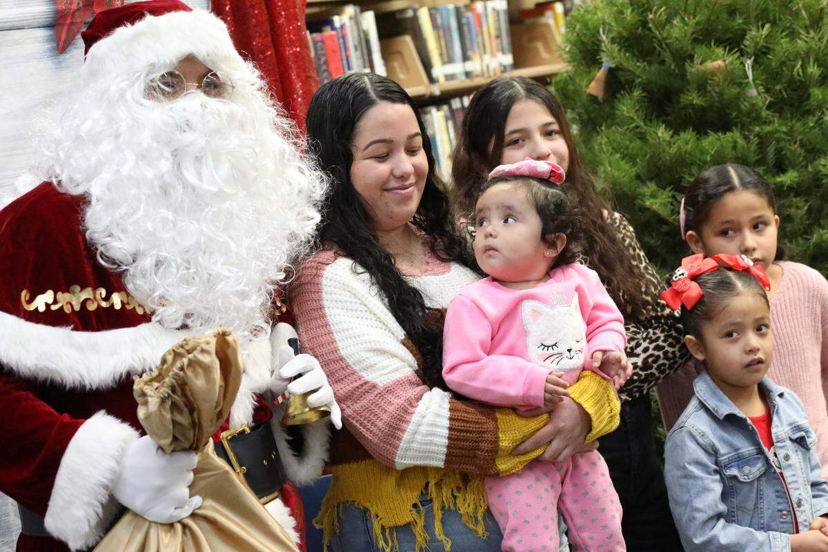 Isela Molina smiles as her 1-year-old Yetzali Ayala (center) takes a close look at Santa during the 2023 Migrant Family Christmas event that took place at Firebaugh High School library on Dec. 13.