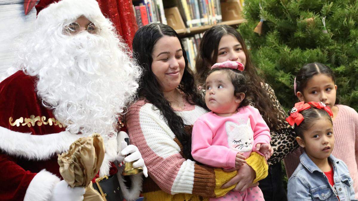 Isela Molina smiles as her 1-year-old Yetzali Ayala (center) takes a close look at Santa during the 2023 Migrant Family Christmas event that took place at Firebaugh High School library on Dec. 13.