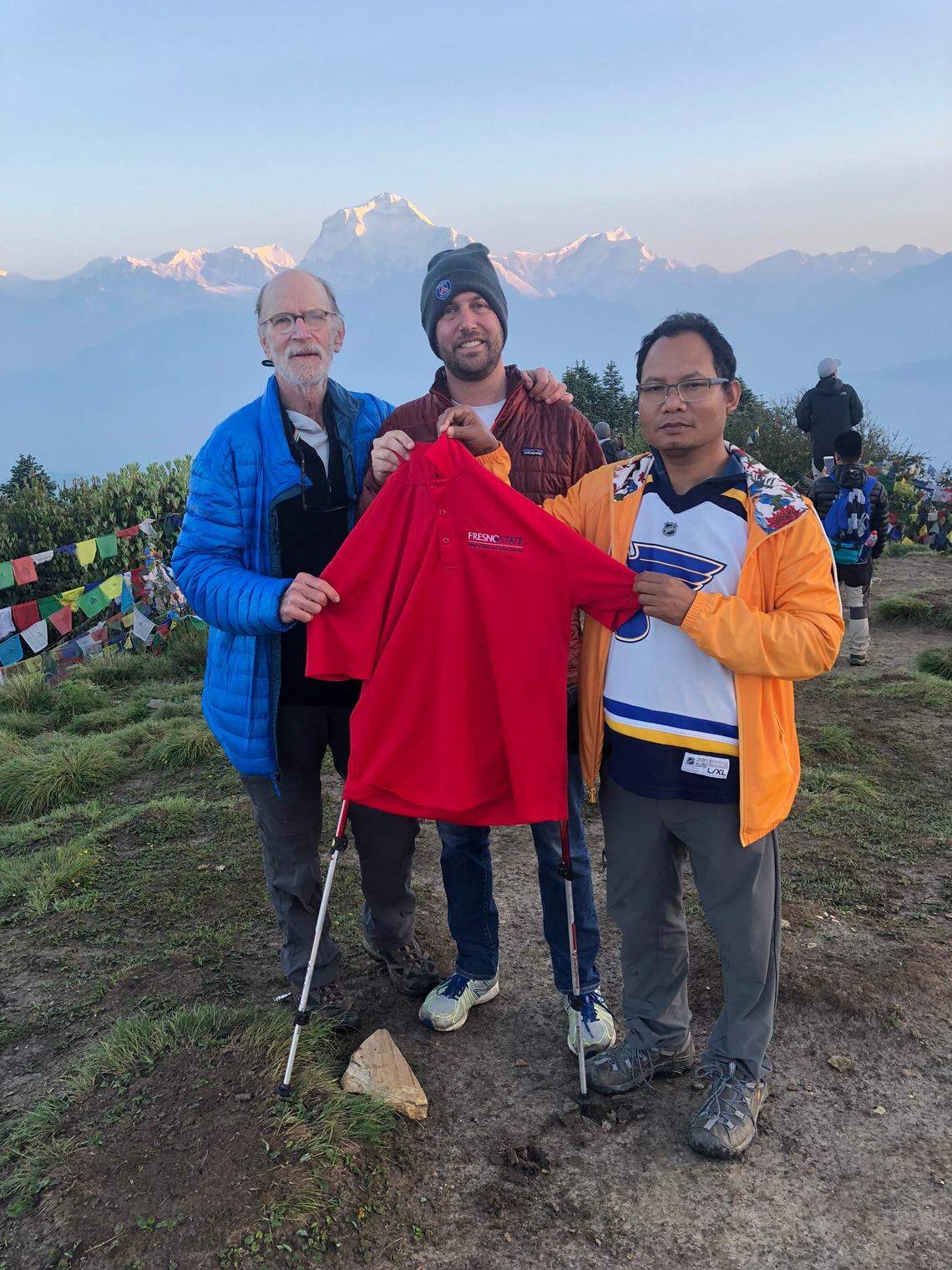 Robert Levine, left, son Andy Levine, center, and Gyanesh Lama hold a Fresno State shirt atop Poon Hill during their recent trip to Nepal.