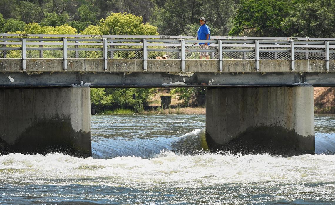 A man walks his dog over a bridge near the Pine Flat Dam as water from the lower Kings River rushes below it on Monday, May 22, 2023. The Fresno County Sheriff’s Office has closed the Kings River due to dangerously high water levels.