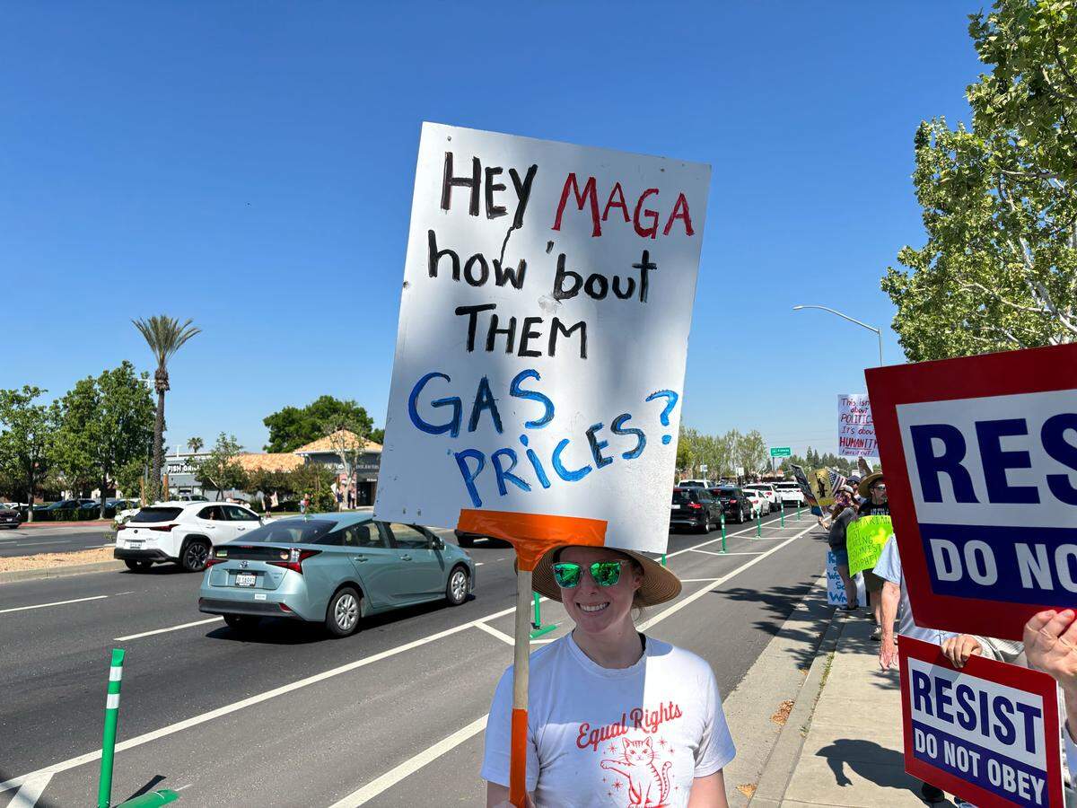 Un manifestante sostiene un cartel sobre los precios de la gasolina en la protesta “No Kings” de Fresno, en Blackstone Avenue cerca de River Park, el sábado 28 de marzo de 2026.
