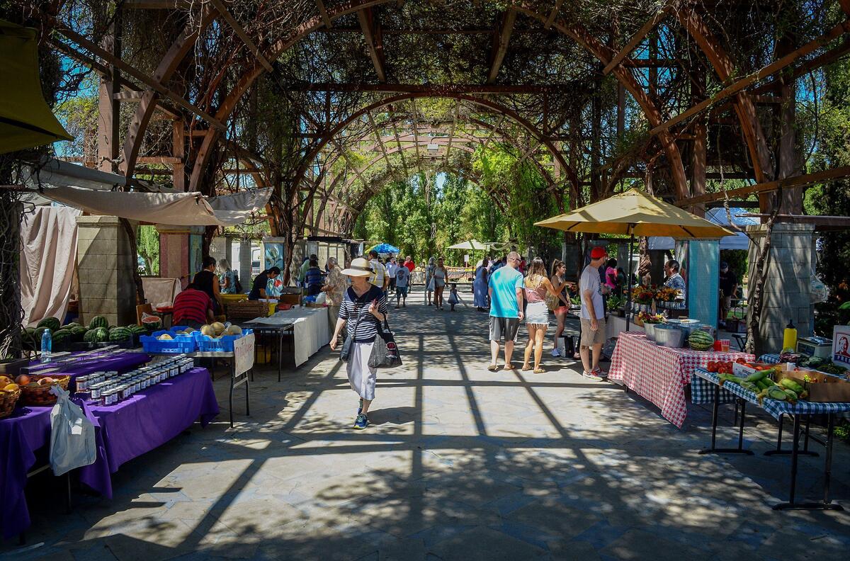 Vendors and customers enjoy a bit of shade from the hot sunshine beneath the large arbor at the Vineyard Farmers Market in Fresno on Saturday, July 27, 2019.