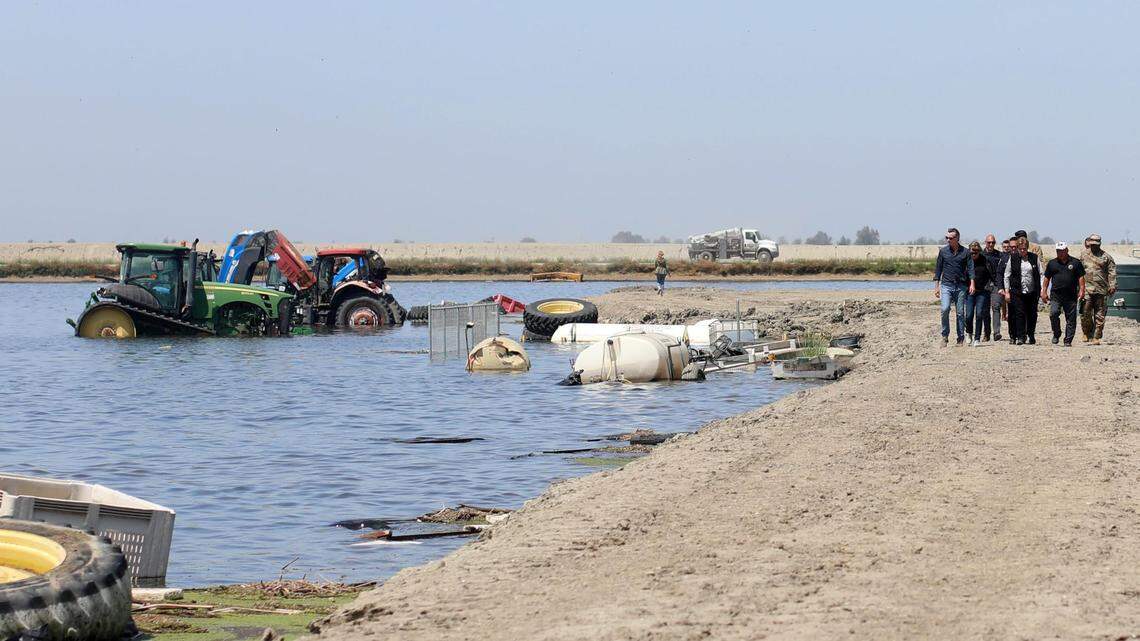 El gobernador de California, Gavin Newsom, extrema izquierda, mira la maquinaria agrícola que está inundada mientras camina sobre un dique en Hansen Ranches en 6th Avenue, el martes 25 de abril de 2023, al sur de Corcoran, CA.
