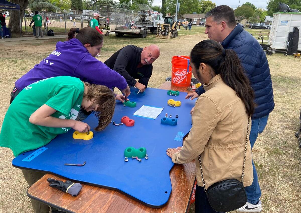 Fresno Mayor Jerry Dyer (back center) and Councilmember Tyler Maxwell (right) help assemble a children’s climbing wall that’s part of a new play structure at Cary Park on April 26, 2025.