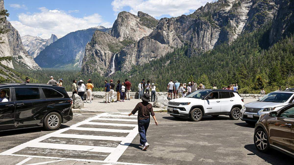 Cars pull into Yosemite National Park's Tunnel View parking lot in search of an open stall as a pedestrian crosses between them to get a look into Yosemite Valley during a busy day in the park on Thursday, May 21, 2026.