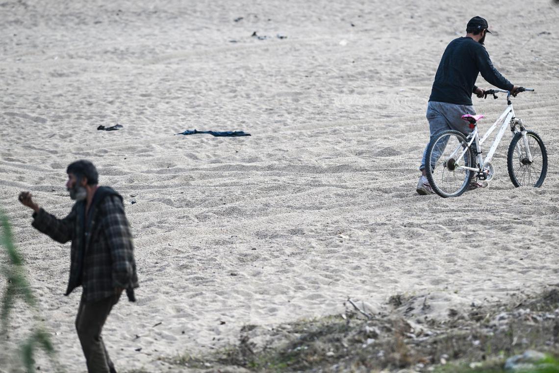 Two men pass each other in the river bottom near the Cleveland Avenue bridge at the Fresno River in Madera where a homeless encampment has been erected on Thursday, Dec. 19, 2024.