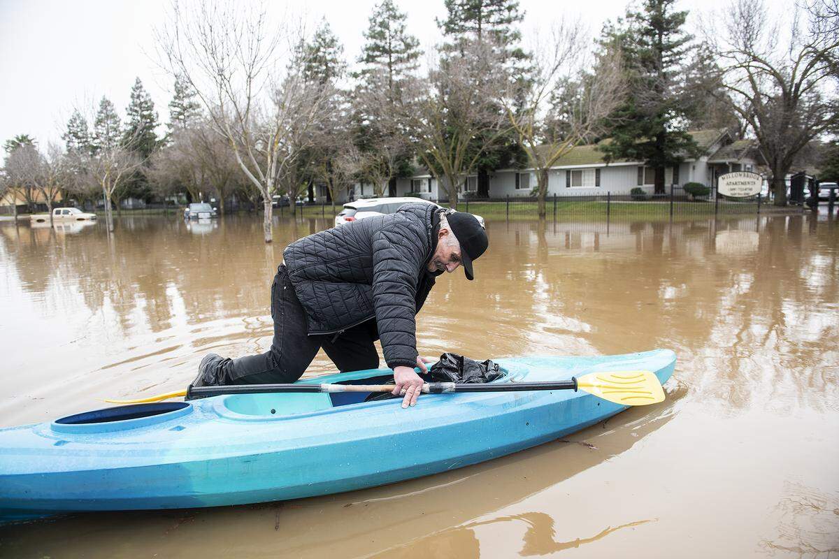 Michael Harrington, 68, climbs into his kayak before navigating through floodwater and back to his residence in the Willowbrook Apartments in Merced, Calif., on Wednesday, Jan. 11, 2023. Harrington said he used the kayak so he could get out of the apartment complex and go to Walmart to buy food.