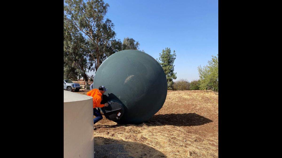 Workers roll a 2,500-gallon water storage tank from Self-Help Enterprises onto a property east of Clovis where a well had gone dry in 2021.