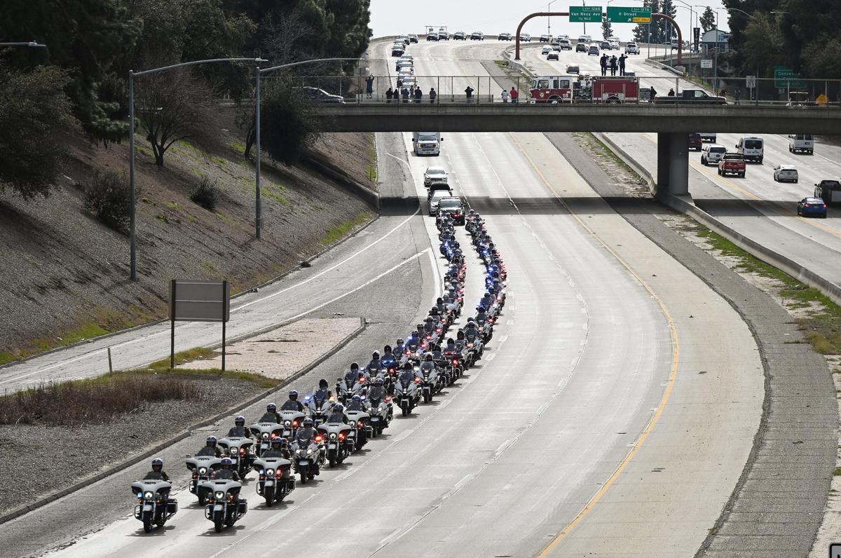 Una caravana de motocicletas de la policía escolta una carroza fúnebre que contiene el ataúd del oficial Gonzalo Carrasco Jr. hacia el norte por la Highway 41 en el centro de Fresno, mientras agentes de todo el estado le siguen en una procesión policial hacia Reedley para el entierro después de un servicio fúnebre en Selland Arena, el jueves 16 de febrero de 2023.
