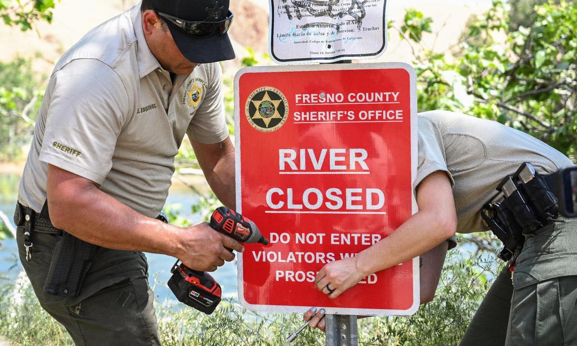 Fresno County Sheriff’s Office reservists attach a sign to a post to alert people that the the Kings River is closed due to dangerously high water levels, on Monday, May 22, 2023.