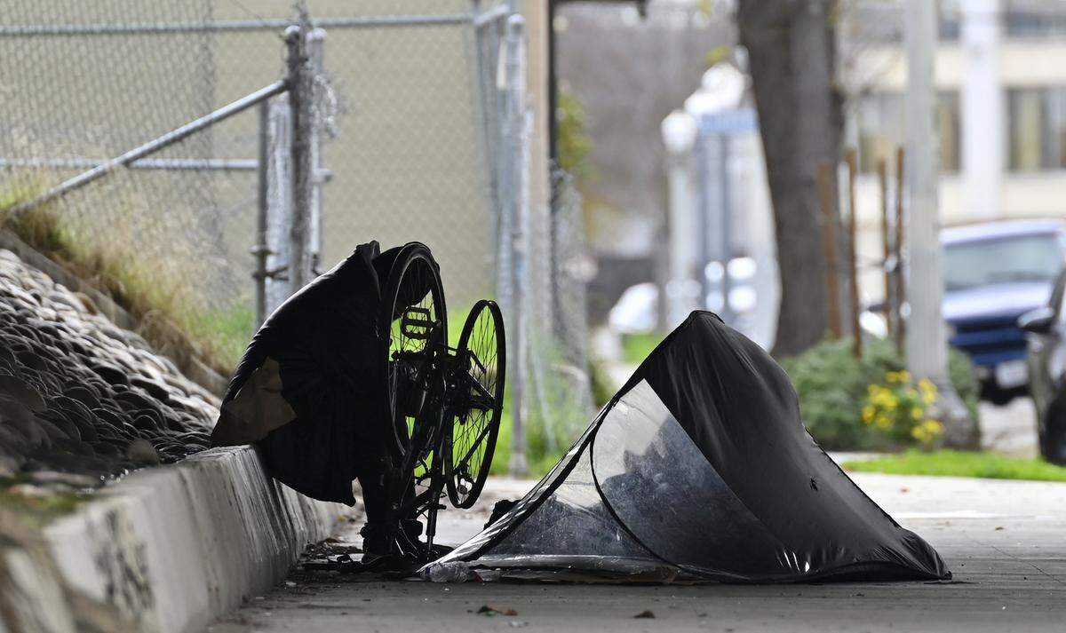A homeless man works on his bicycle outside his tent underneath Freeway 180 on North Broadway Street Friday, Dec 26, 2025 in Fresno.