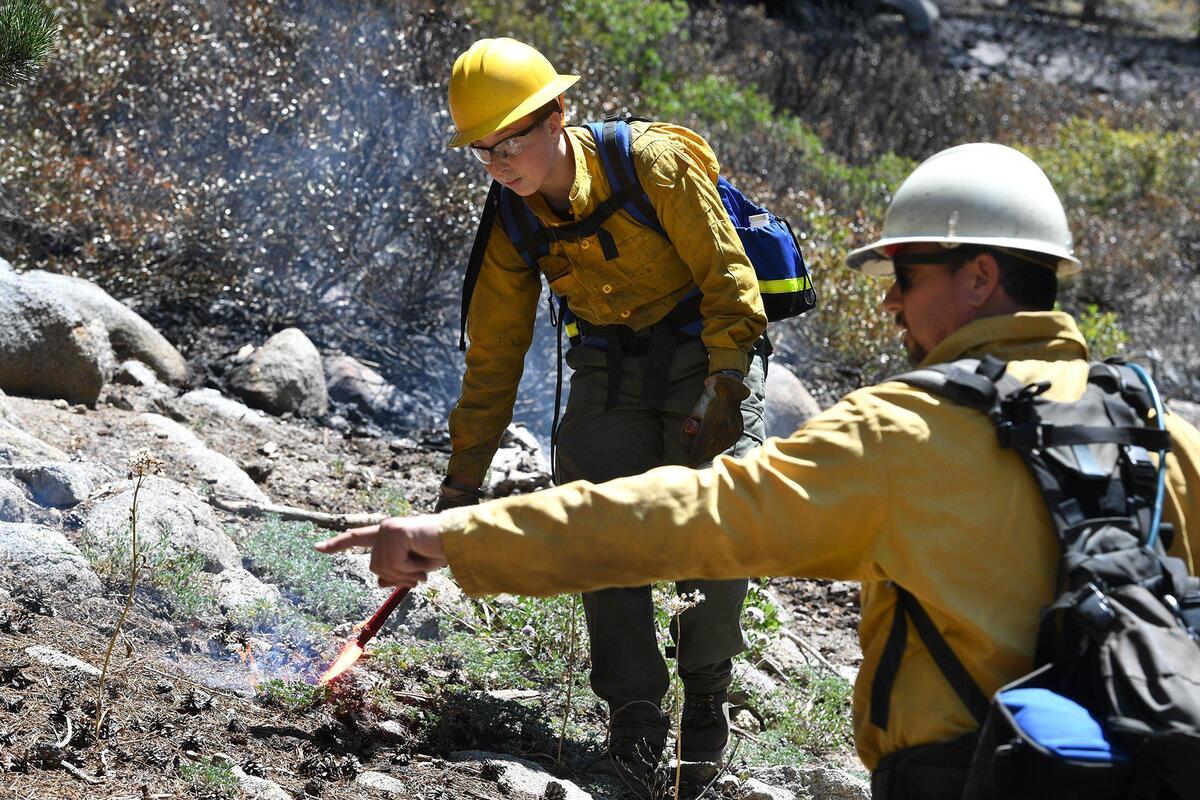 Rosa Wiedenhoft, a Yosemite Women’s Fire Internship member, receives instruction on setting a back-burn with a fuse (a flare-type ignitor), from Kelly Singer, Deputy Fire Management Officer, Yosemite National Park, during the County Line Fire, July 14, 2021.