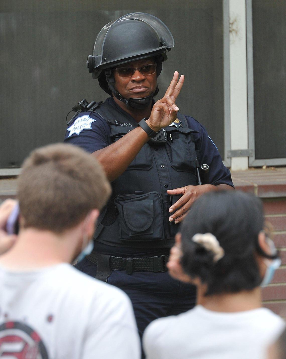Fresno Police officer Katrina Lloyd flashes a peace sign to protesters as they pass police headquarters, Sunday afternoon, May 31, 2020.