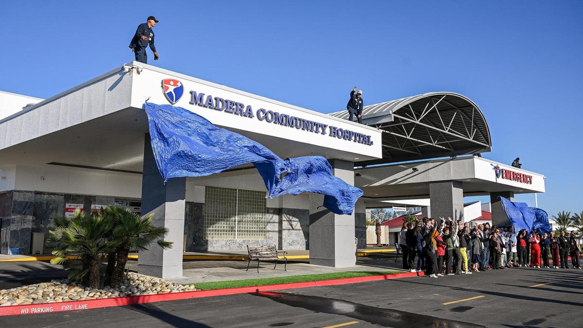 Hospital staff, administrators, and local legislators gather in front of the emergency entrance at Madera Community Hospital in Madera as tarps are dropped to reveal the new signs for the hospital during its reopening on Tuesday, March 18. 2025.