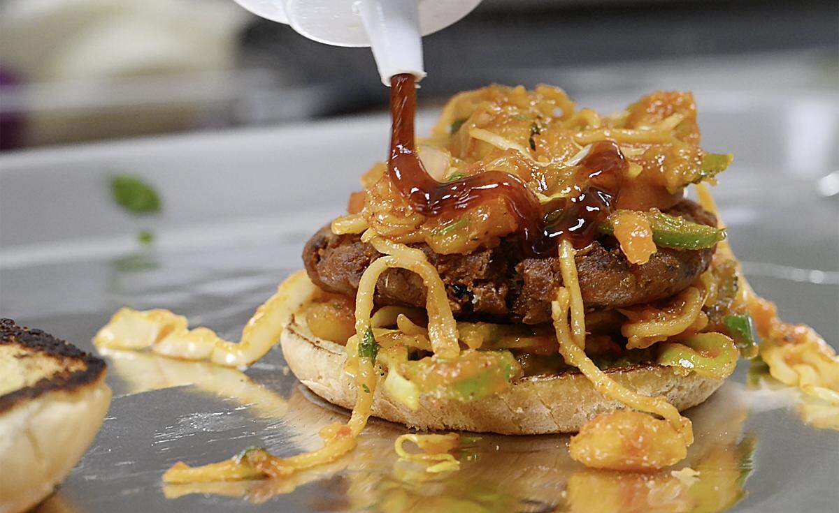 Sweet and Sour Sauce is added to an Aloo Tikka Noodle Burger at Rangla Punjab Restaurant & Sweets Friday, Oct. 17, 2025 in Fresno.