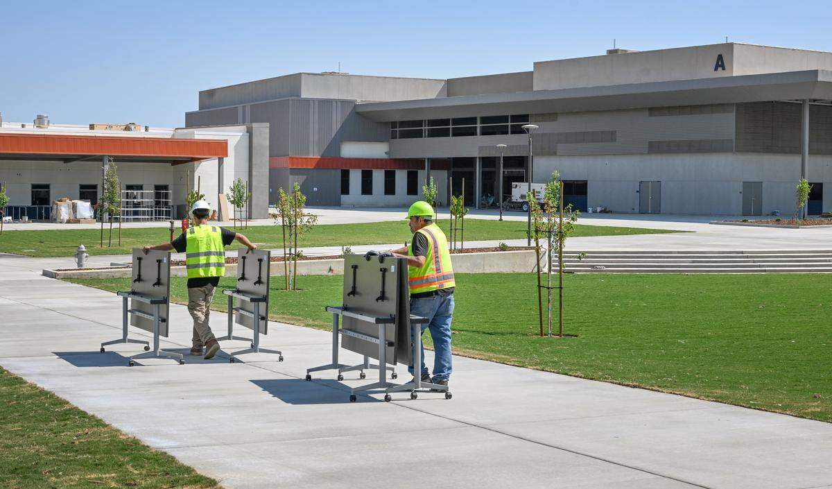 Construction workers push classroom tables across the center quad area near the amphitheater at the Terry P. Bradley Educational Center, on Friday, Aug. 8, 2025 just days before the start of classes on August 18. 