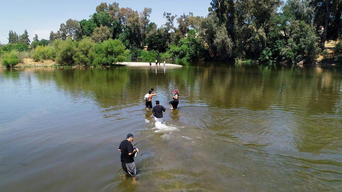 A group of young people wades through the water to a sand bar at Reedley Beach in Reedley on Wednesday, June 6, 2018. Police say a man died Wednesday, Aug. 5, 2020 after trying to rescue two children in the area of Reedley Beach.
