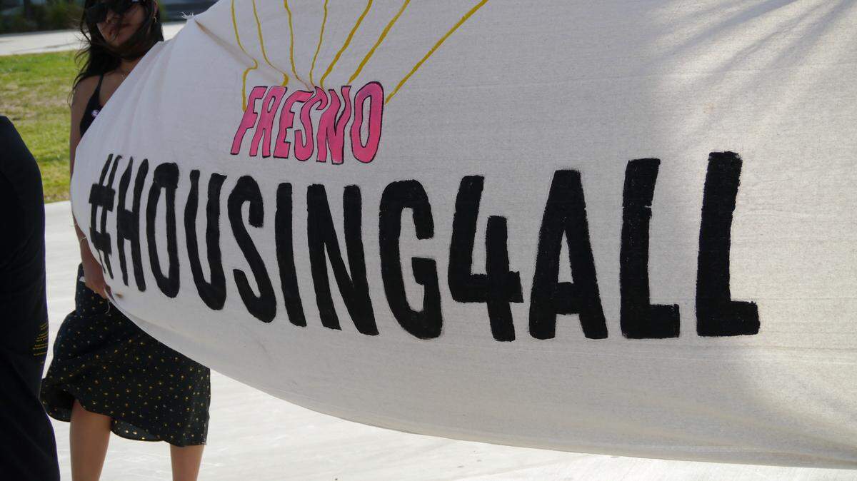 Karla Martinez, a policy advocate for Leadership Counsel for Justice and Accountability, holds a #HousingforAll banner at the State of the People of the City event at the Cultural Arts Park in downtown Fresno on May 19, 2022.