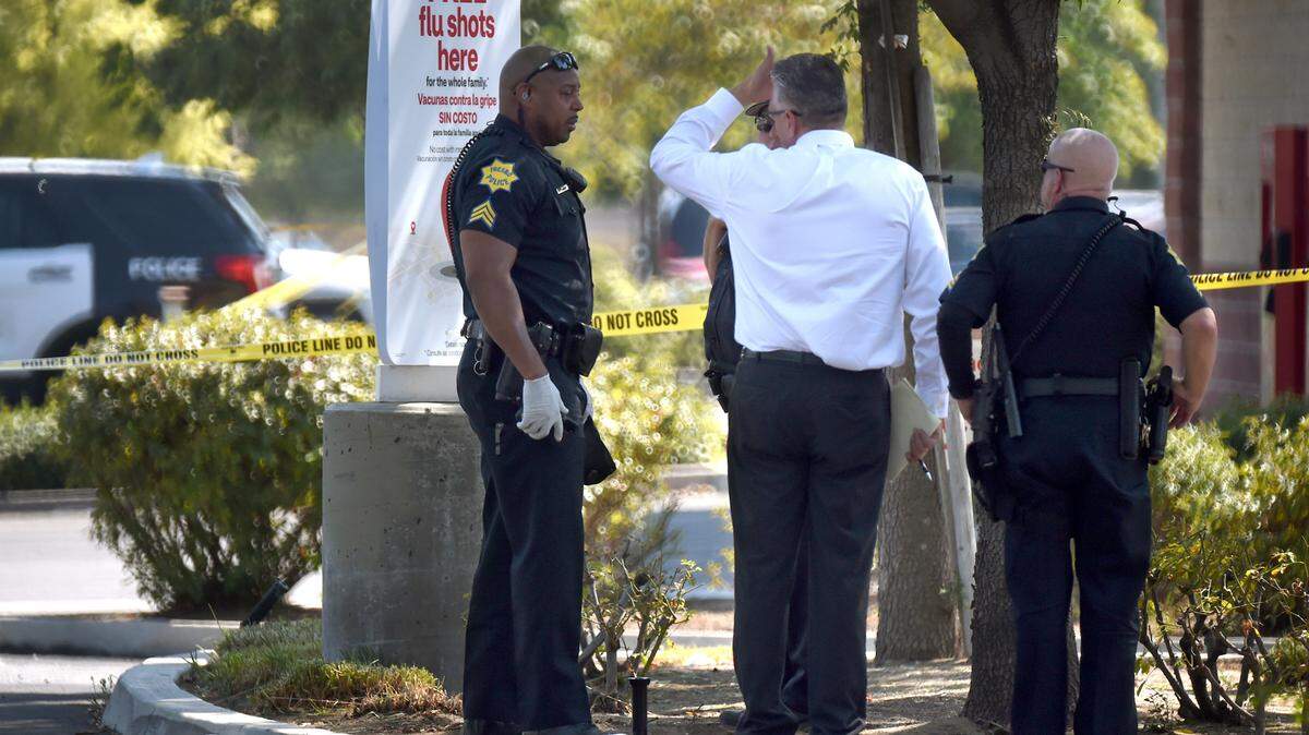A Fresno Police detective, center, and officers confer in the parking lot of the Peach Tree Plaza shopping center, across from Sunnyside High, as they investigate a shooting Friday afternoon, Aug. 28, 2020.